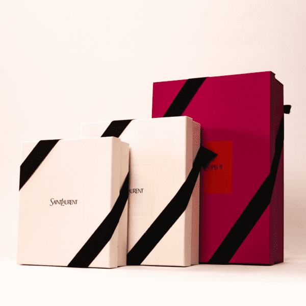 Three gift boxes of varying sizes, two in off-white and one in red, each tied with a black ribbon