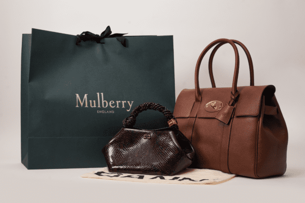 A dark green Mulberry shopping bag with the brand name "Mulberry England" in gold lettering, alongside a small brown snakeskin handbag with a twisted handle and a larger brown leather handbag with a flap closure and gold hardware.