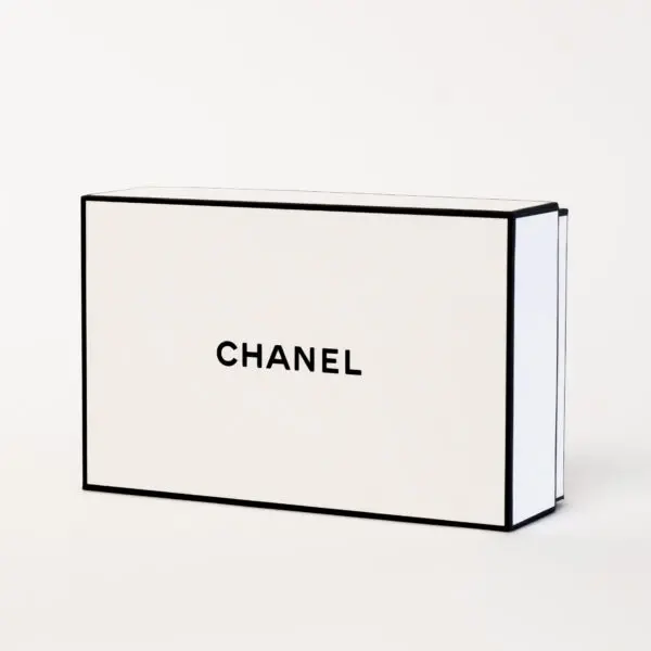 A rectangular white Chanel box with black trim and the word "CHANEL" printed