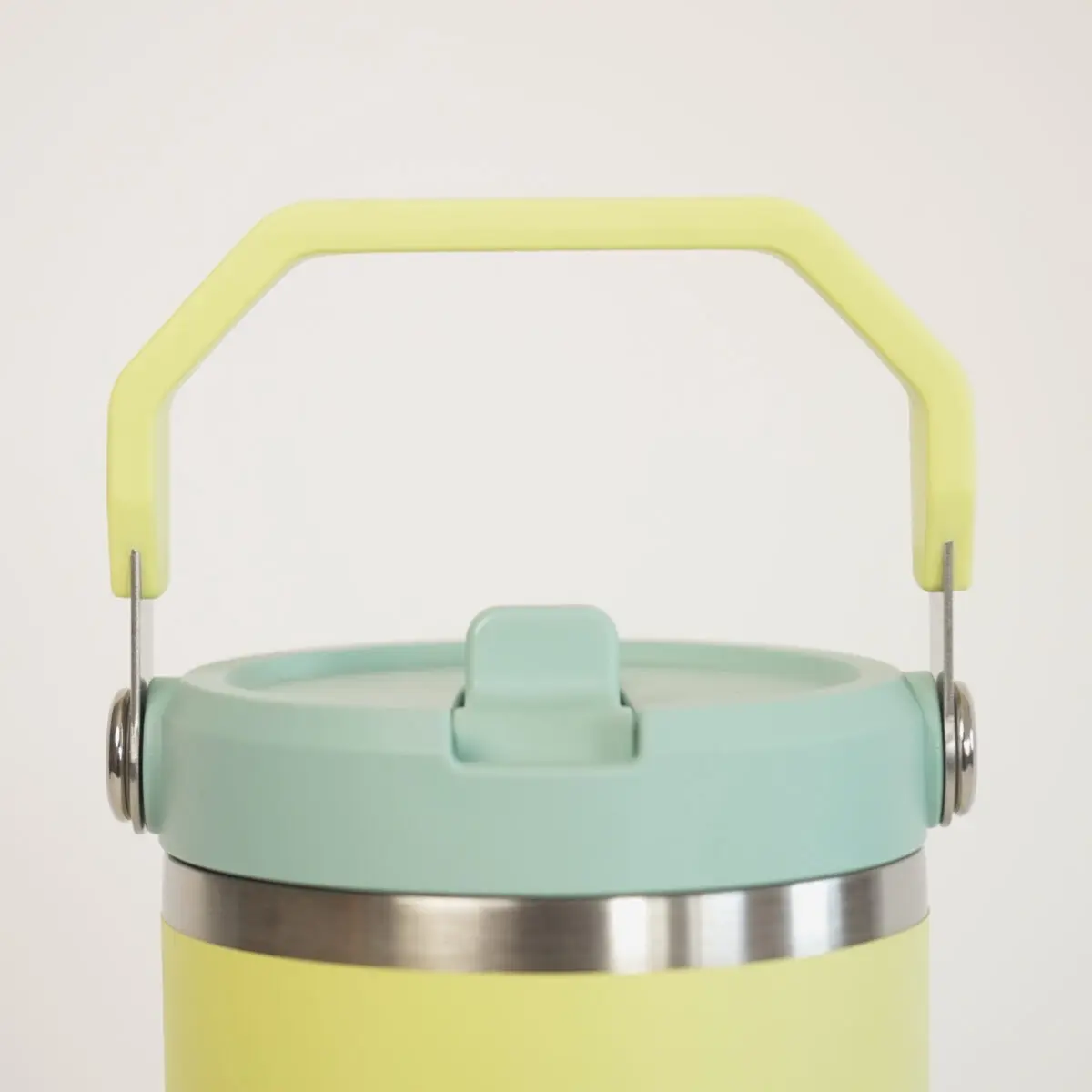 A close-up shows the top of a two-toned Stanley tumbler. The body is light yellow, topped with a pale mint green lid, and a bright, light green handle