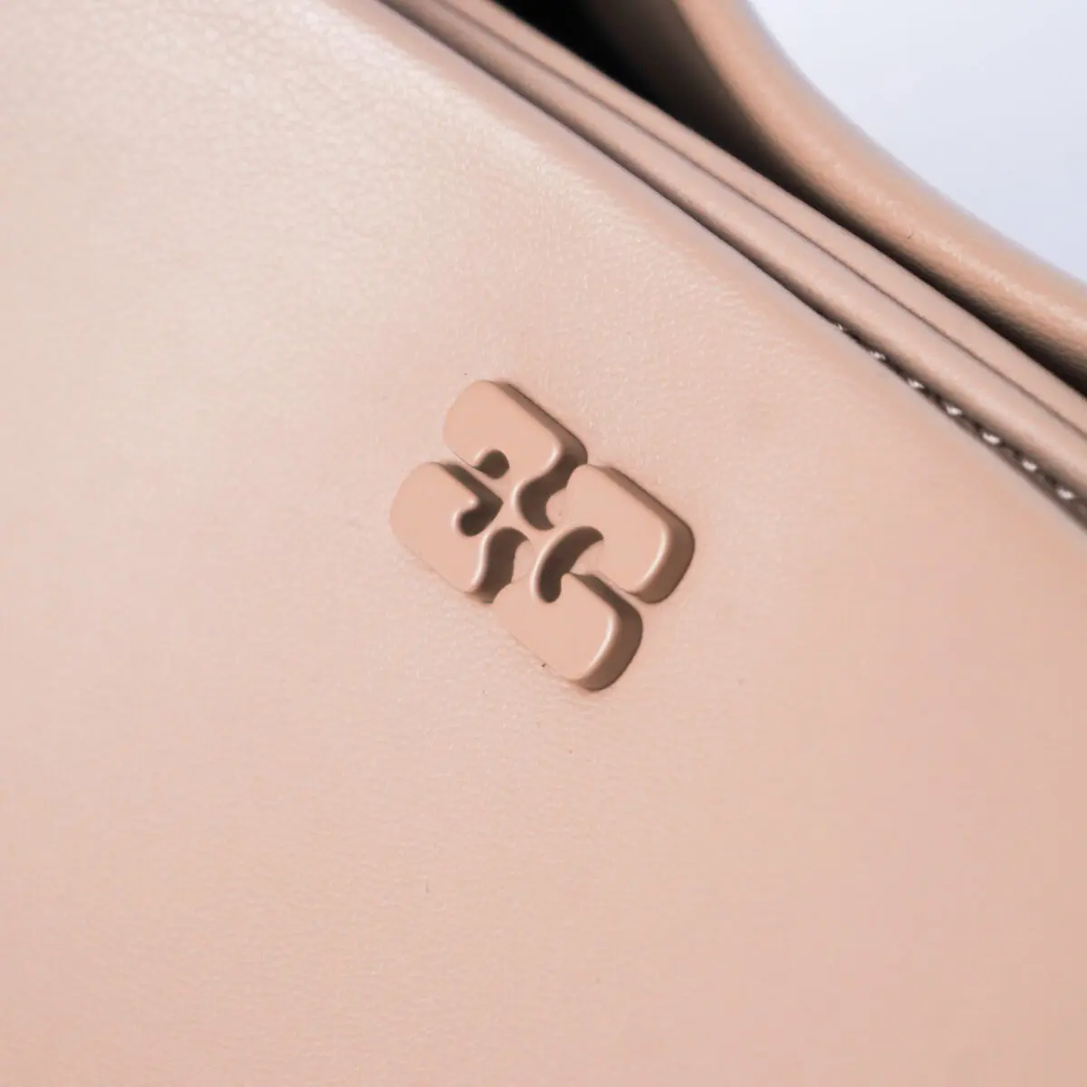 Close-up of a light pink handbag with a raised, abstract logo on its surface