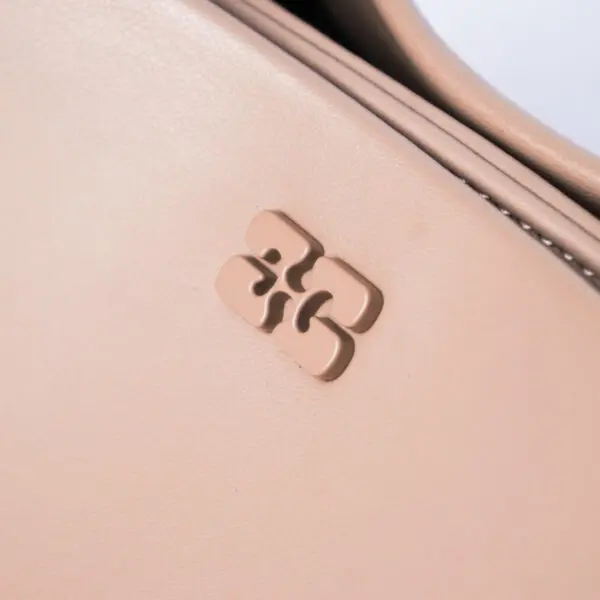 Close-up of a light pink handbag with a raised, abstract logo on its surface